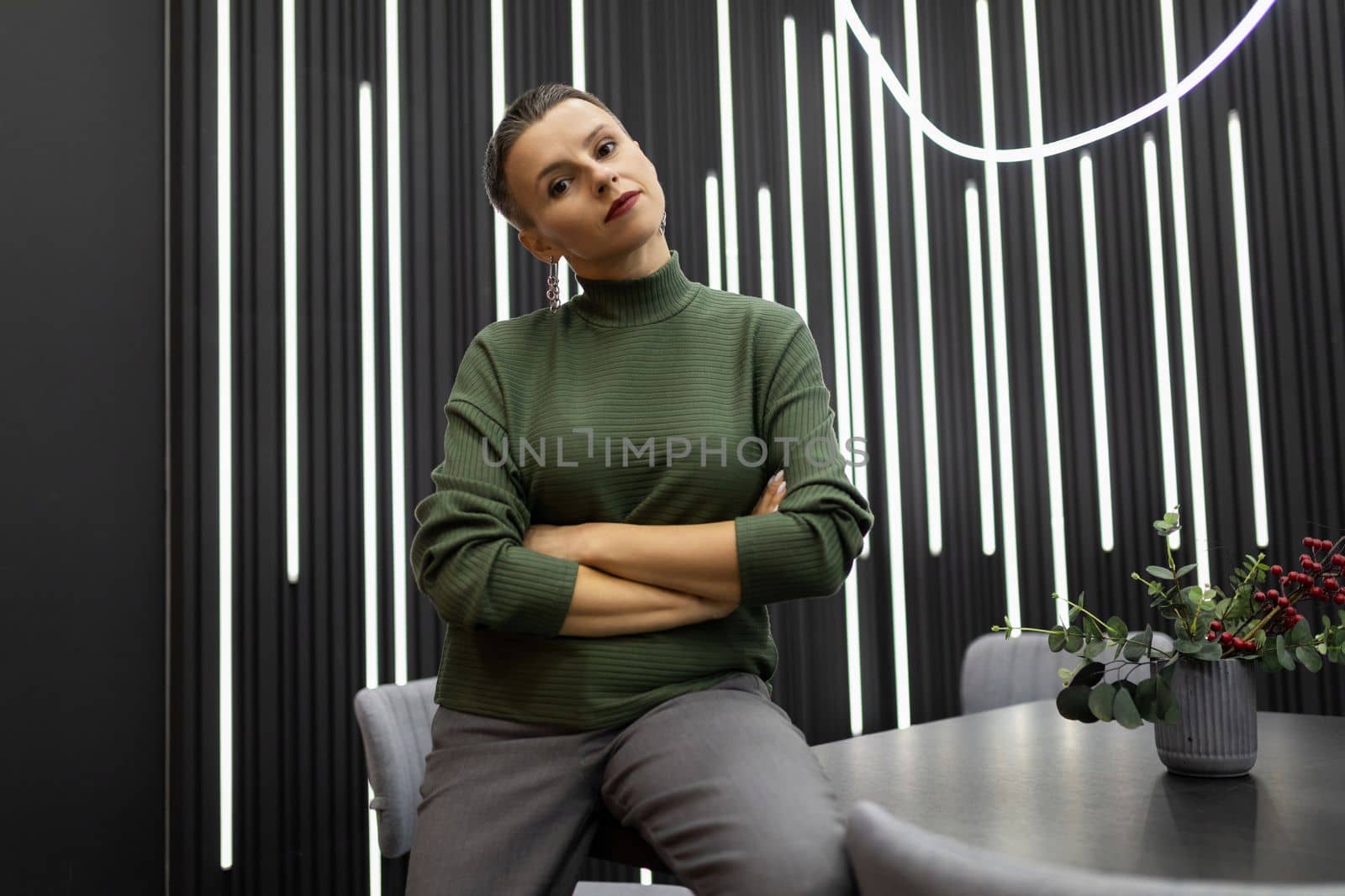 serious thoughtful business woman sits leaning on the table with her arms crossed over her chest by TRMK