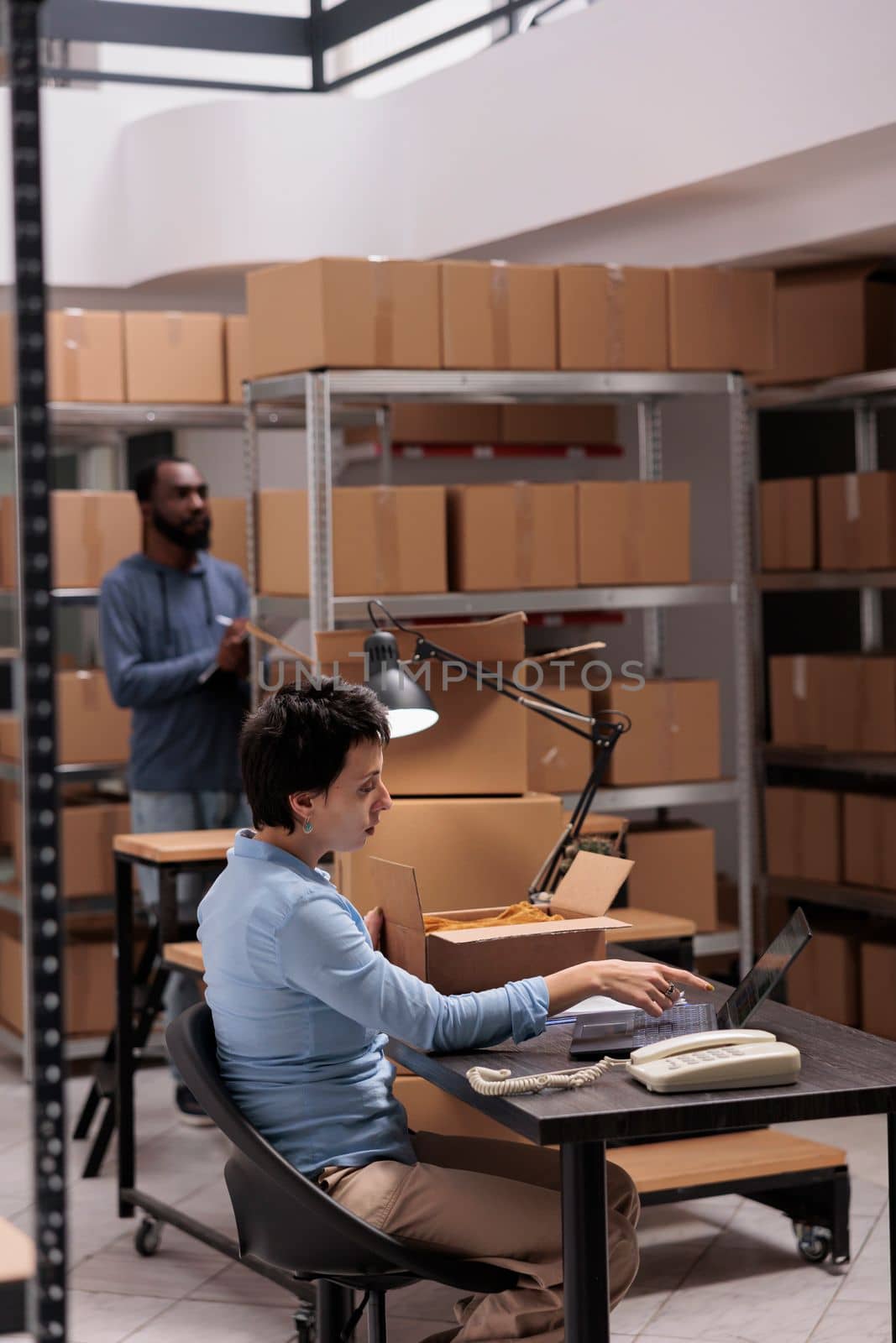 Woman supervisor looking at cargo stock on laptop computer while checking fashion blouse status before start preparing clients packages. Employee working at warehouse delivery department