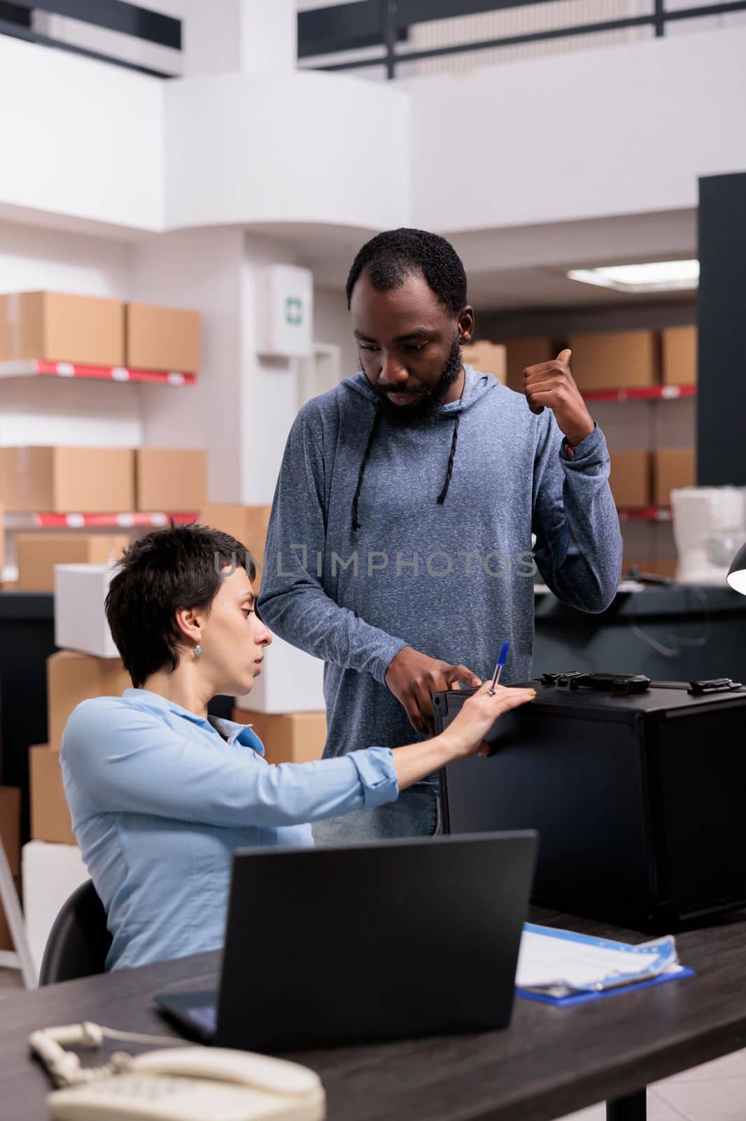 Storehouse delivery workers checking metallic box looking at package order while working at packaging production in warehouse. Multi ethnic team analyzing shipment logistics on laptop computer