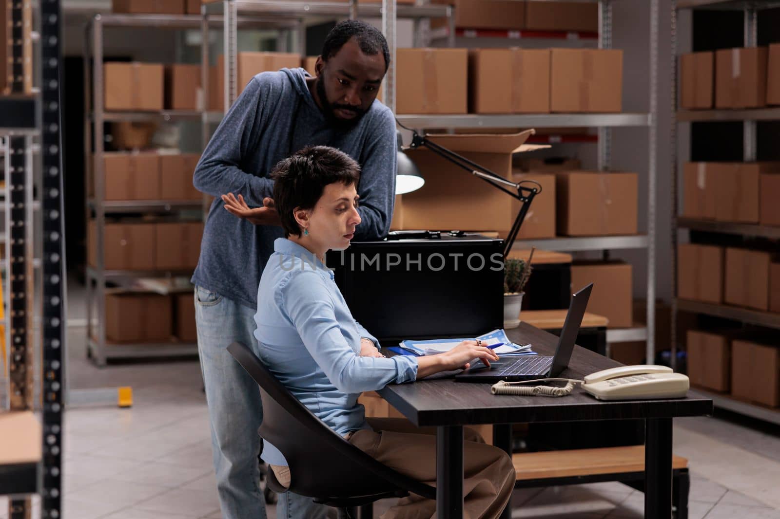 Warehouse workers analyzing checklist on laptop computer searching for metallic box order by DCStudio