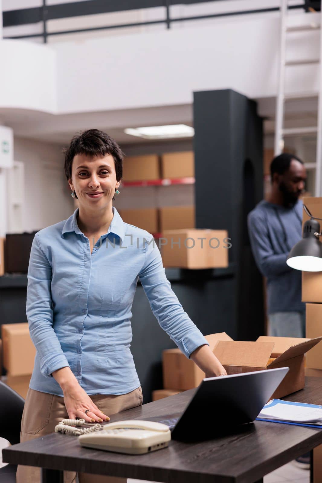 Smiling manager working in warehouse delivery department checking clients shipping details after preparing packages. Team putting customers orders in carton boxes using bubble wrap for protection