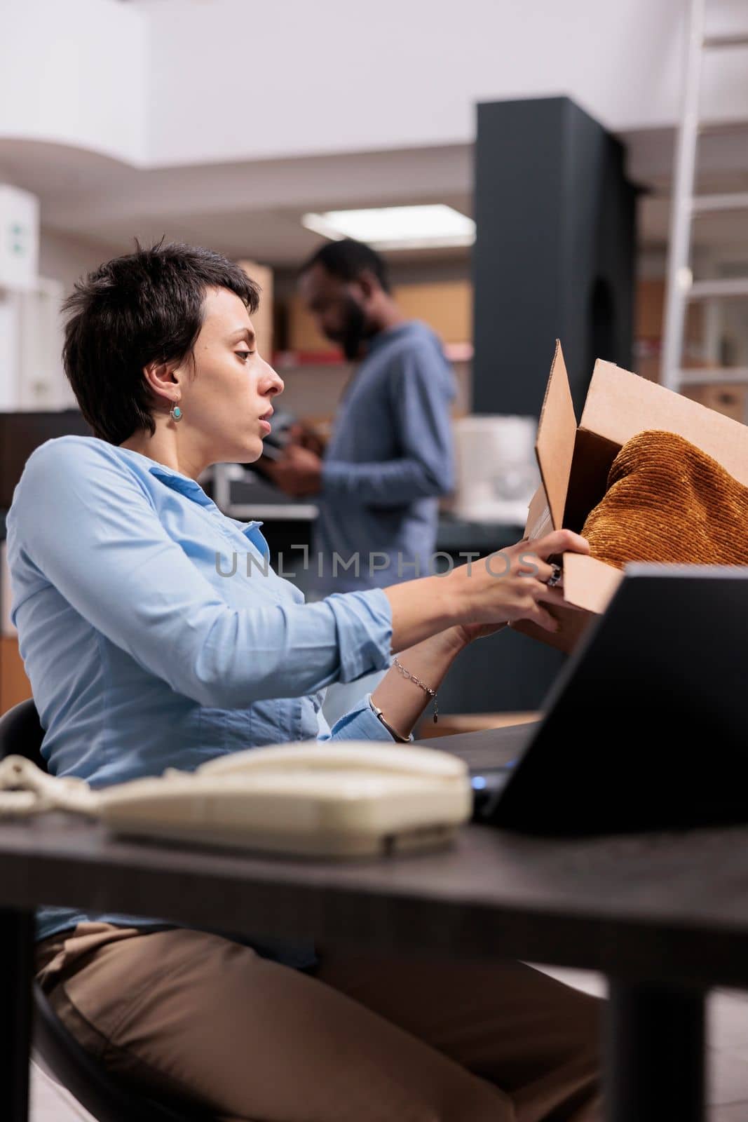Storehouse employee looking at cardboard box checking shipping details before start preparing customer packages for delivering. Woman analyzing cargo stock on laptop computer working in warehouse