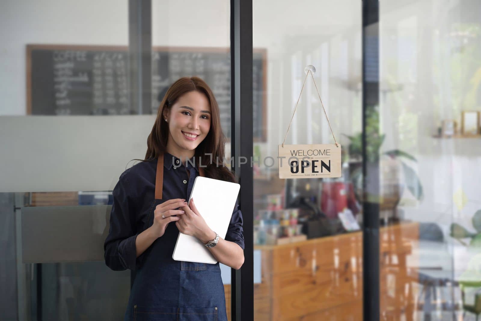 Smiling female waitress holding digital tablet and standing in modern coffee shop.