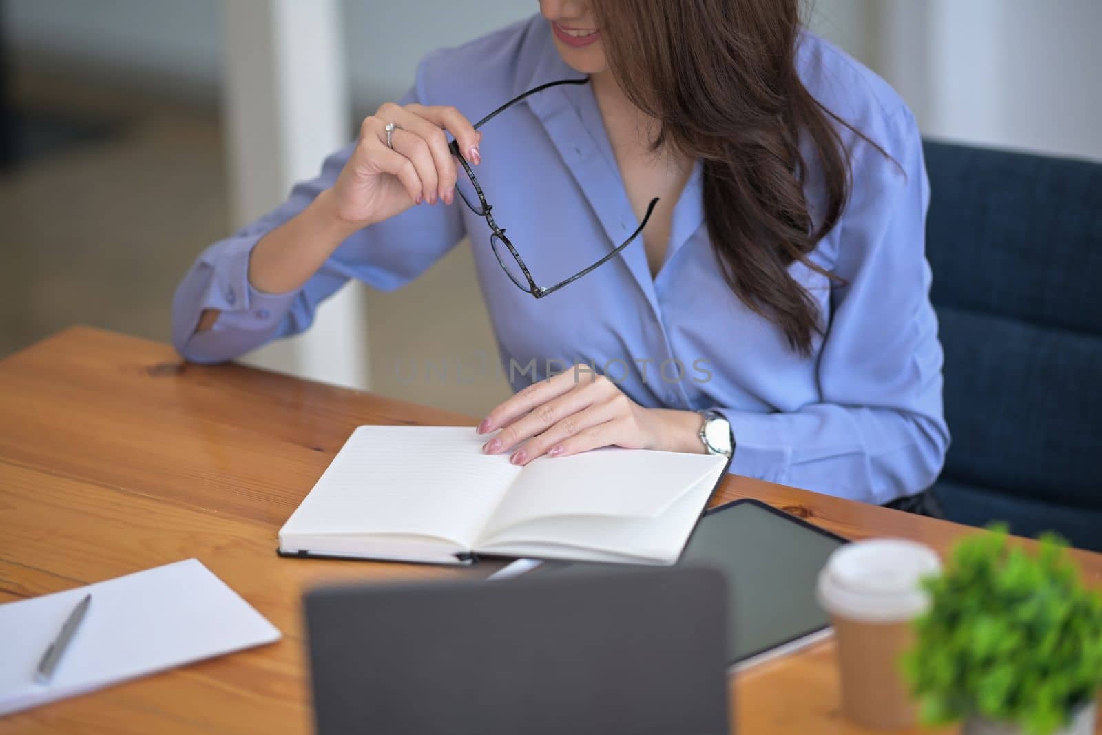 Businesswoman holding her eyeglasses and reading a book at her office desk.