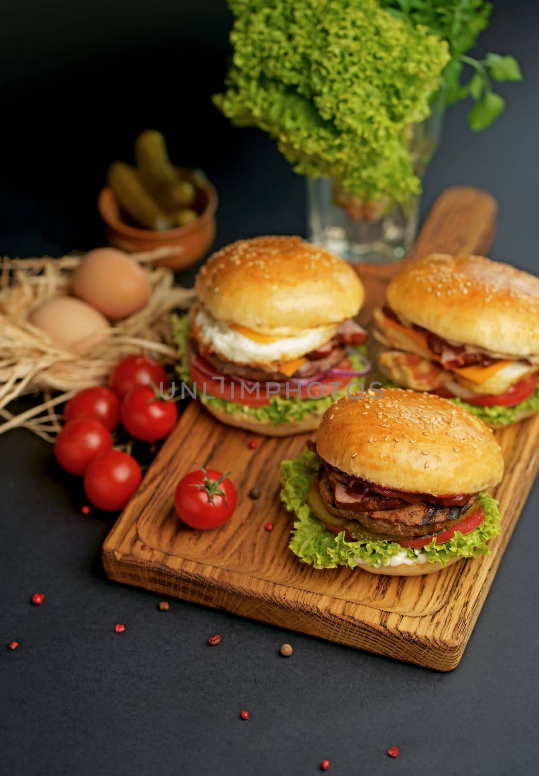 Homemade tasty double burger with beef, salad, bacon, tomatoes and cheese on wooden background. Rustic style.