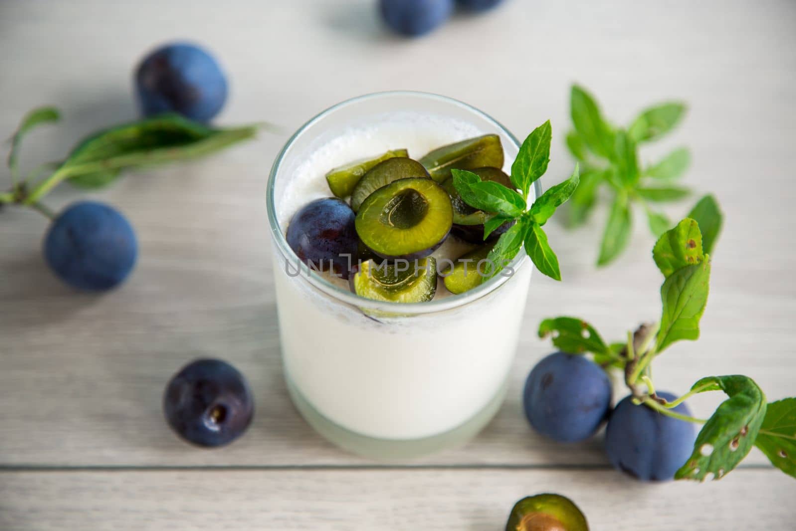 sweet homemade yogurt with fresh plum slices in a glass on a wooden table