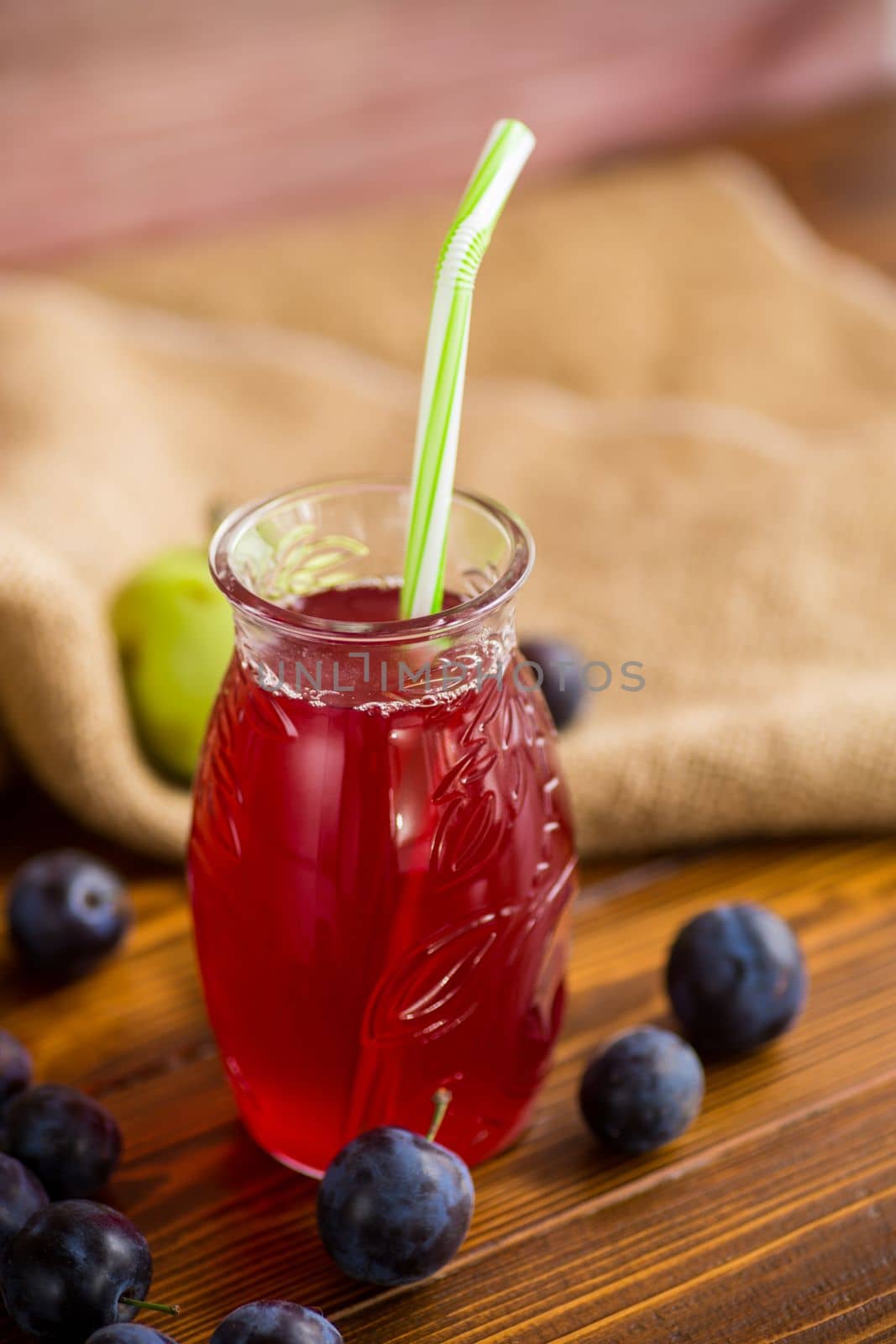 Sweet natural plum drink in a glass with a straw on a wooden table