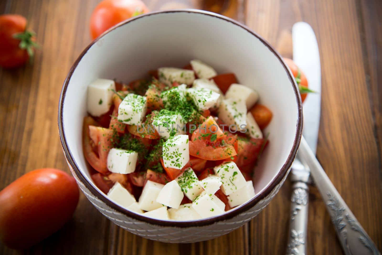 salad of fresh ripe tomatoes with mozzarella and spices in a bowl on a wooden table