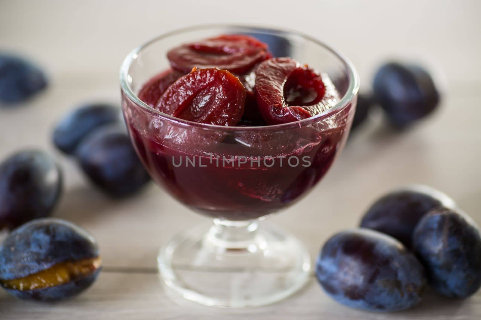 Sweet plums in syrup, in a glass bowl on a wooden table.
