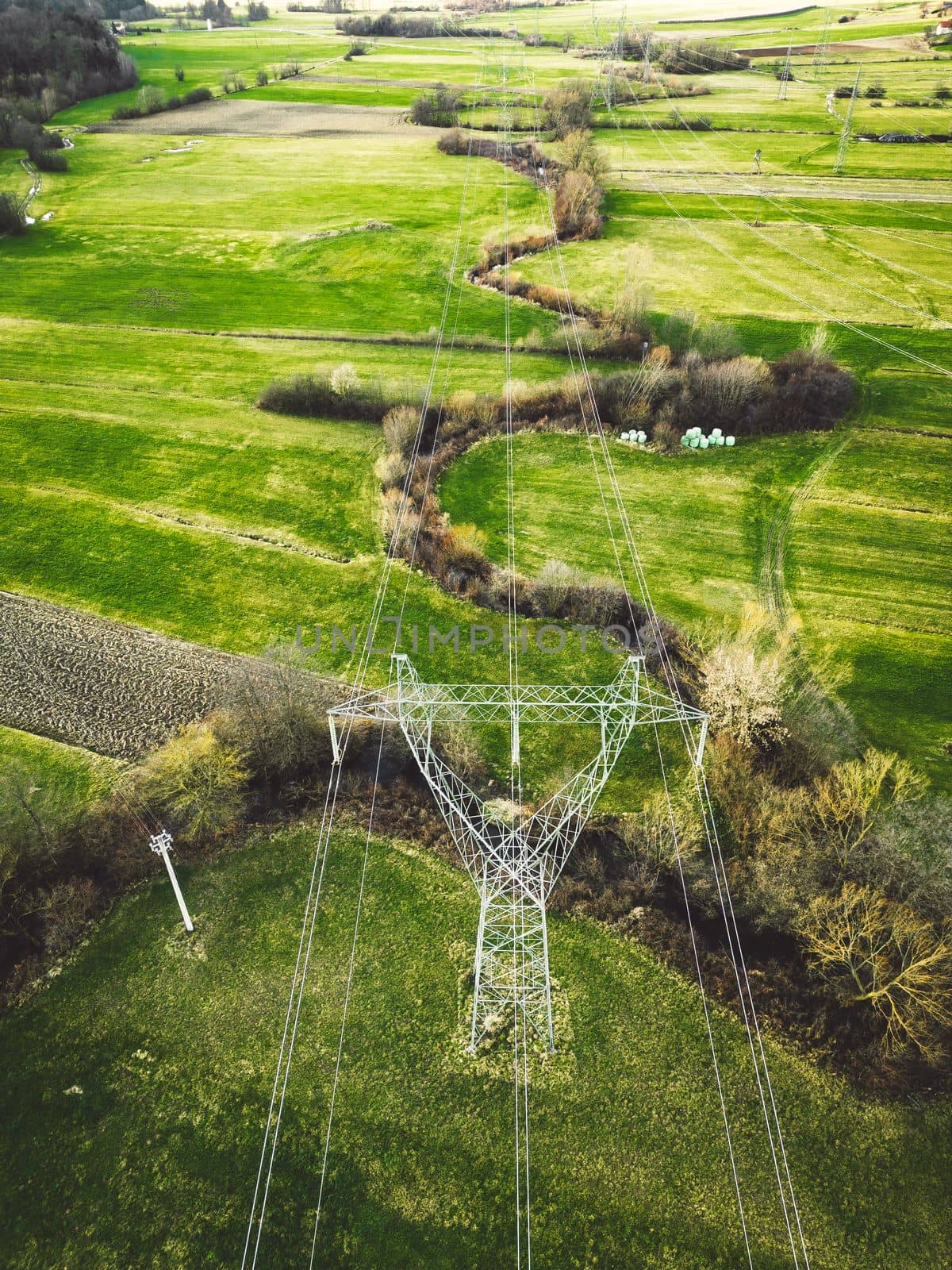 Vertical photo directly above centered on the electrical tower an electrical wires running from it across the green country side of Slovenia by VisualProductions