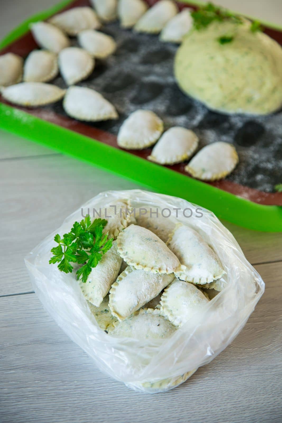 Raw green dough dumplings with parsley, dill. Raw dumplings in a bag on a wooden table.