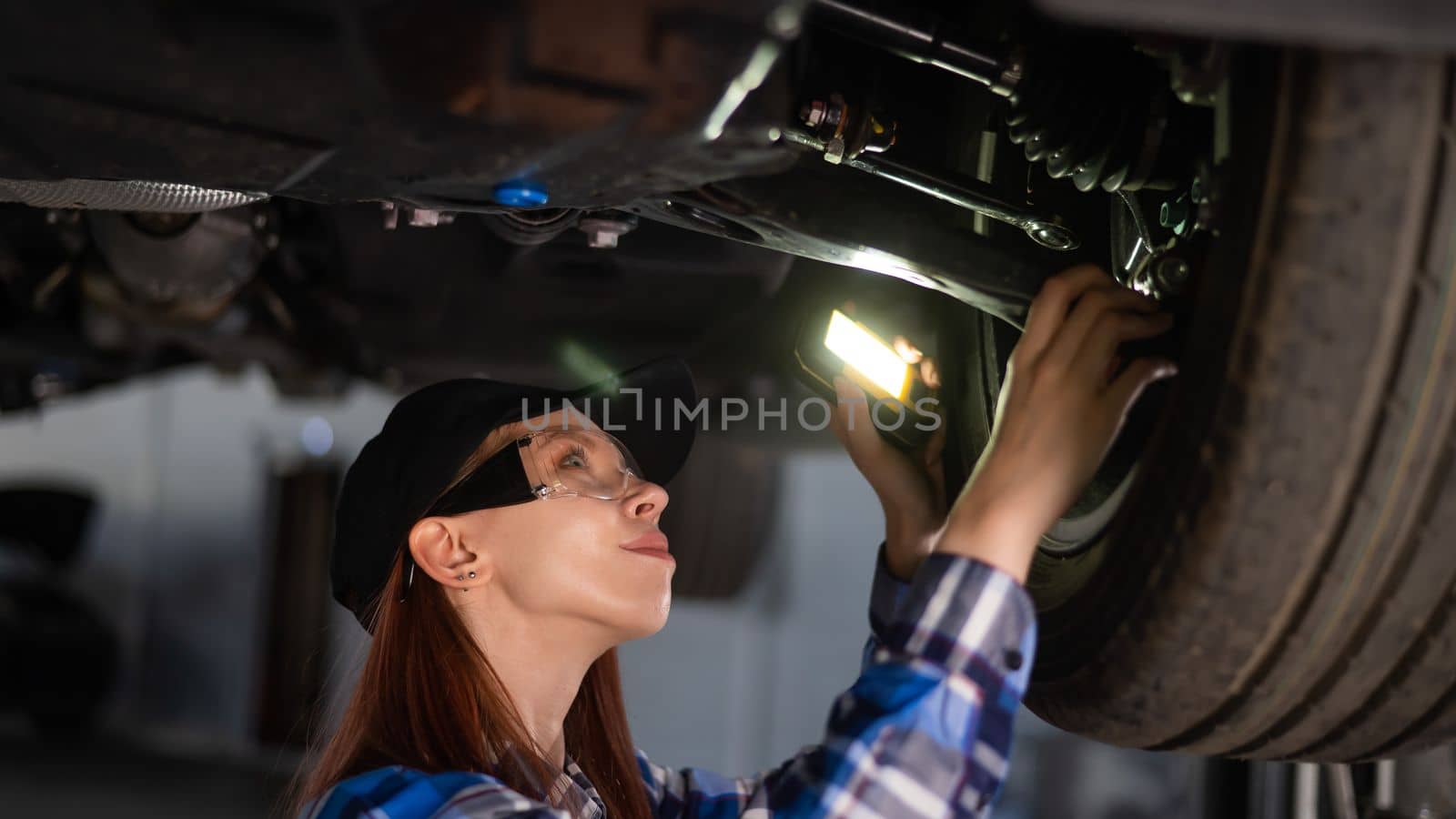 A female mechanic inspects a lifted car. A girl at a man's work. by mrwed54