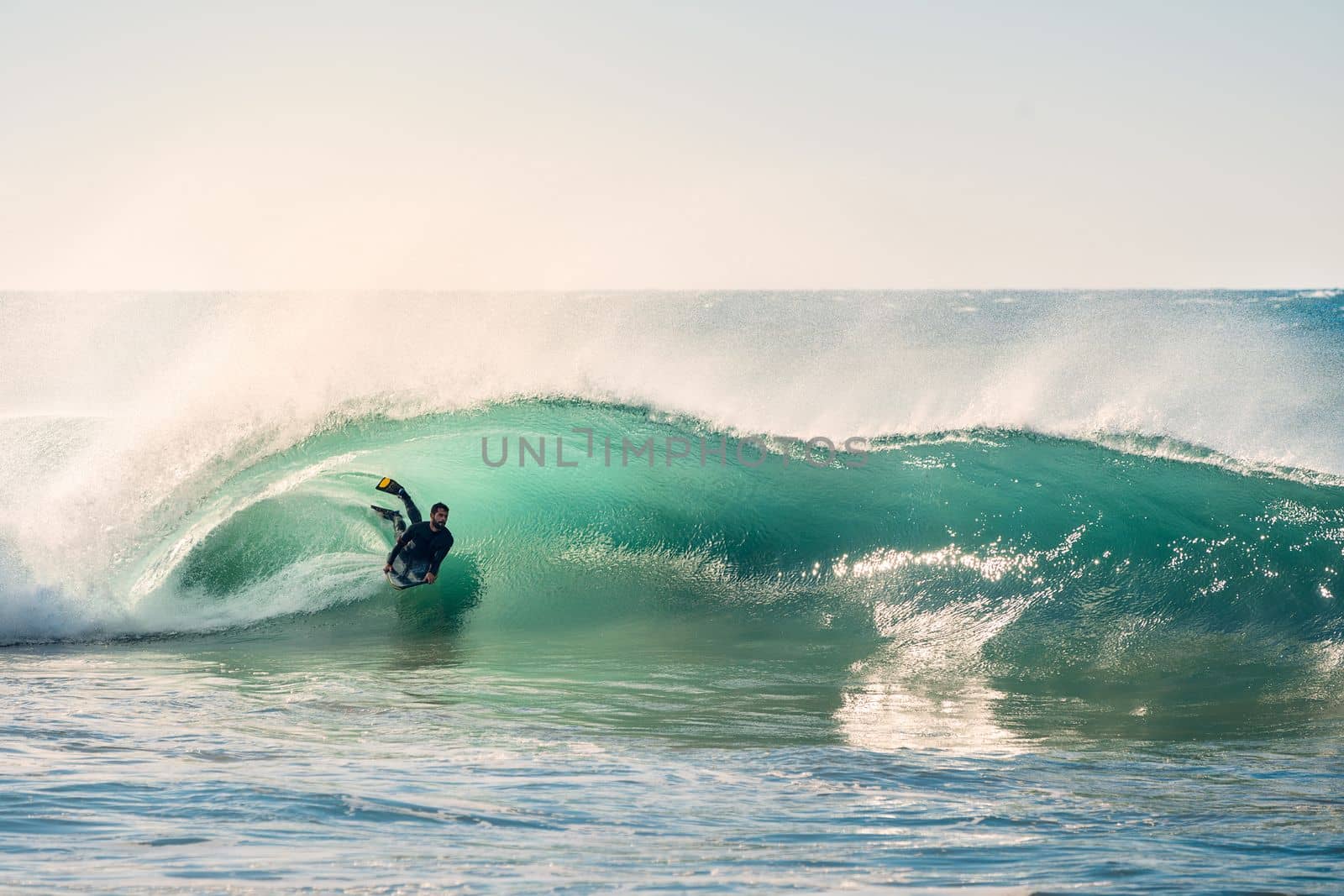 man surfing rides in the barrel of a beautiful wave that breaks with energy and power, sunlight reflects golden on the turquoise surface of the sea and in the foam, the wind rises columns of water