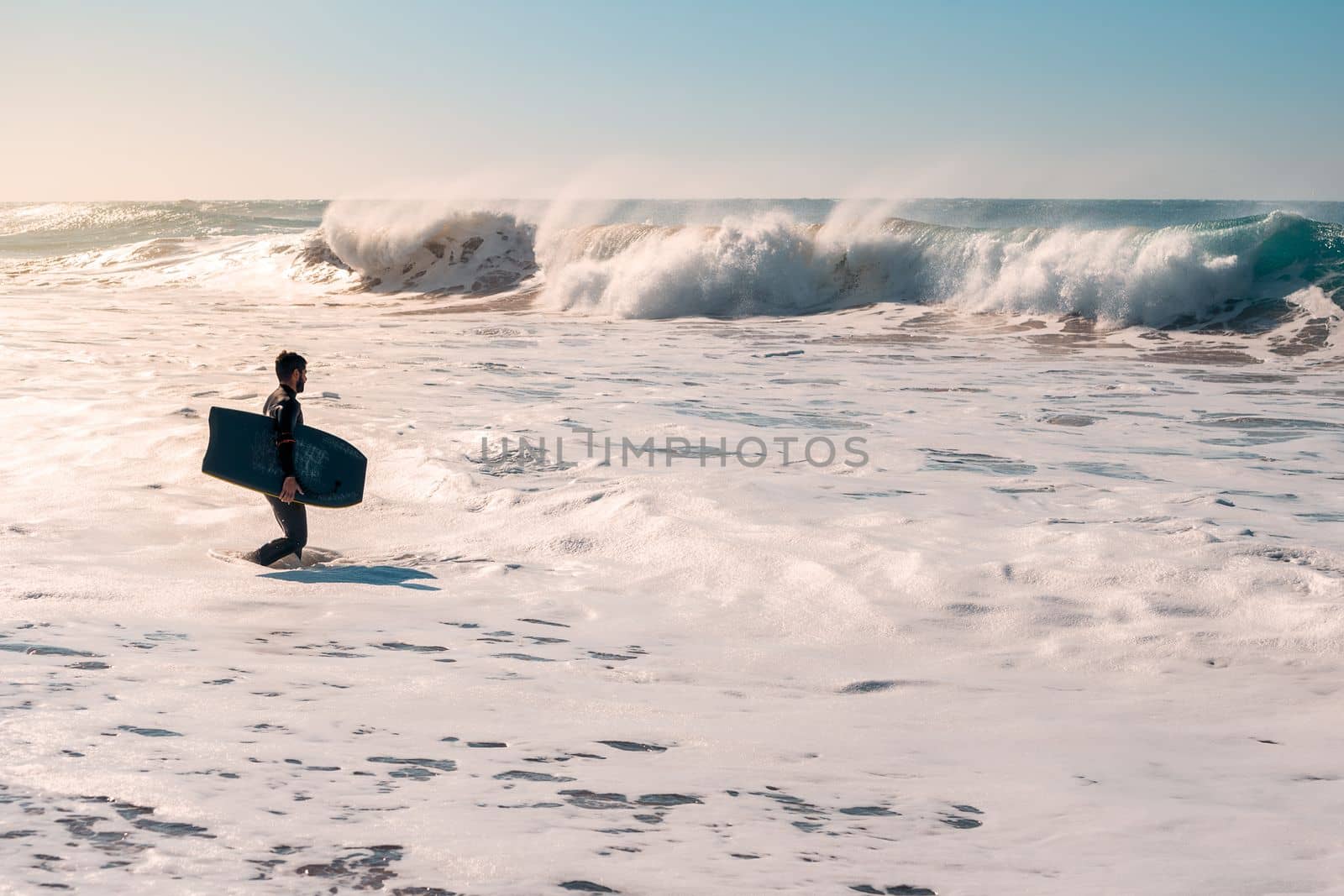 Surfer walks at dawn looking a big wave breaking by raulmelldo