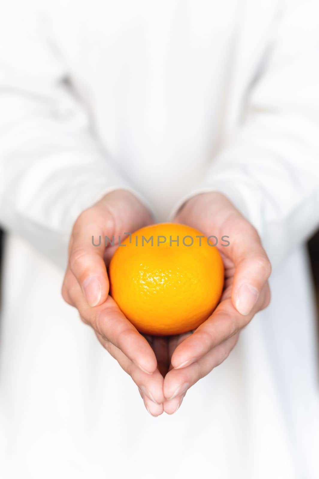 A girl in a white sweater holds a fresh sweet tangerine against the background of herself in defocus. Close-up.