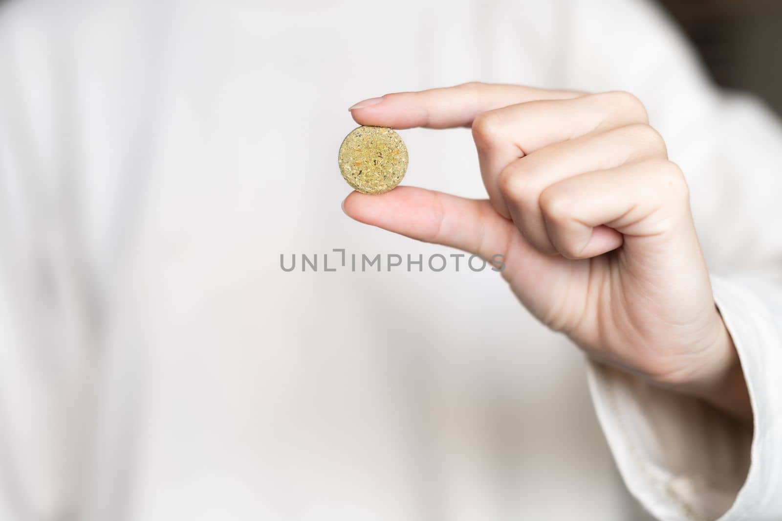 Close-up of a woman holding a pill, a herbal capsule in her hand against the background of a white sweater in blur.