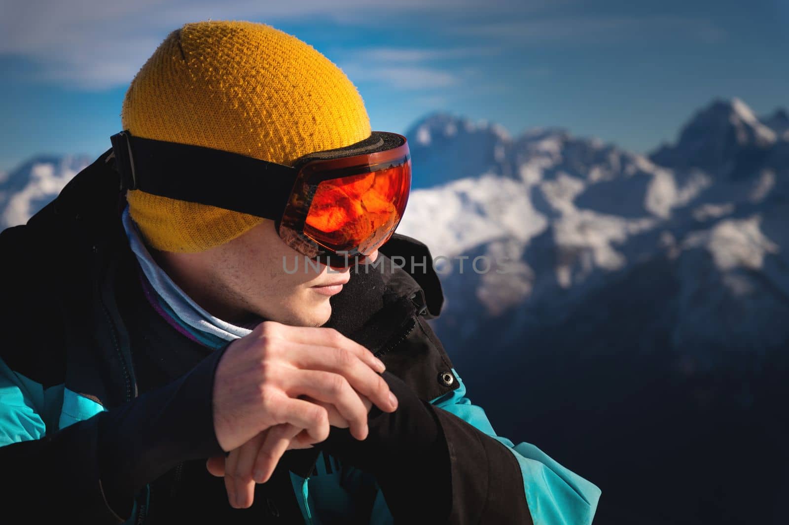 Portrait in profile of a male skier on a mountain, against the backdrop of snow-capped mountains and blue sky.