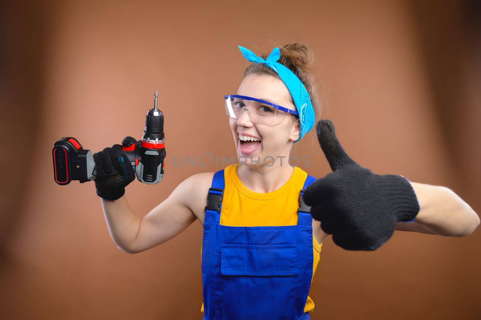 Young smiling practical woman working with screwdriver showing thumbs up gesture. Portrait of a builder or handyman with a screwdriver in his hand.