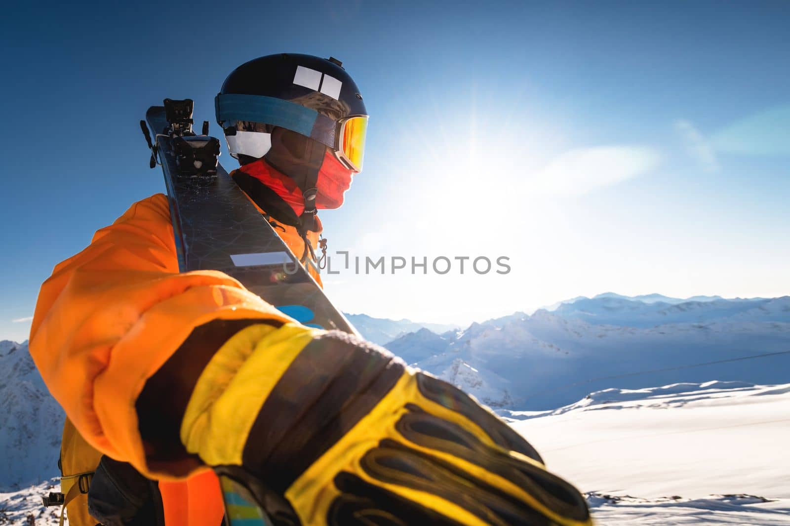 skier in the winter mountains against the backdrop of a sunny sky, wide angle from below, a man holds skis on his shoulder.