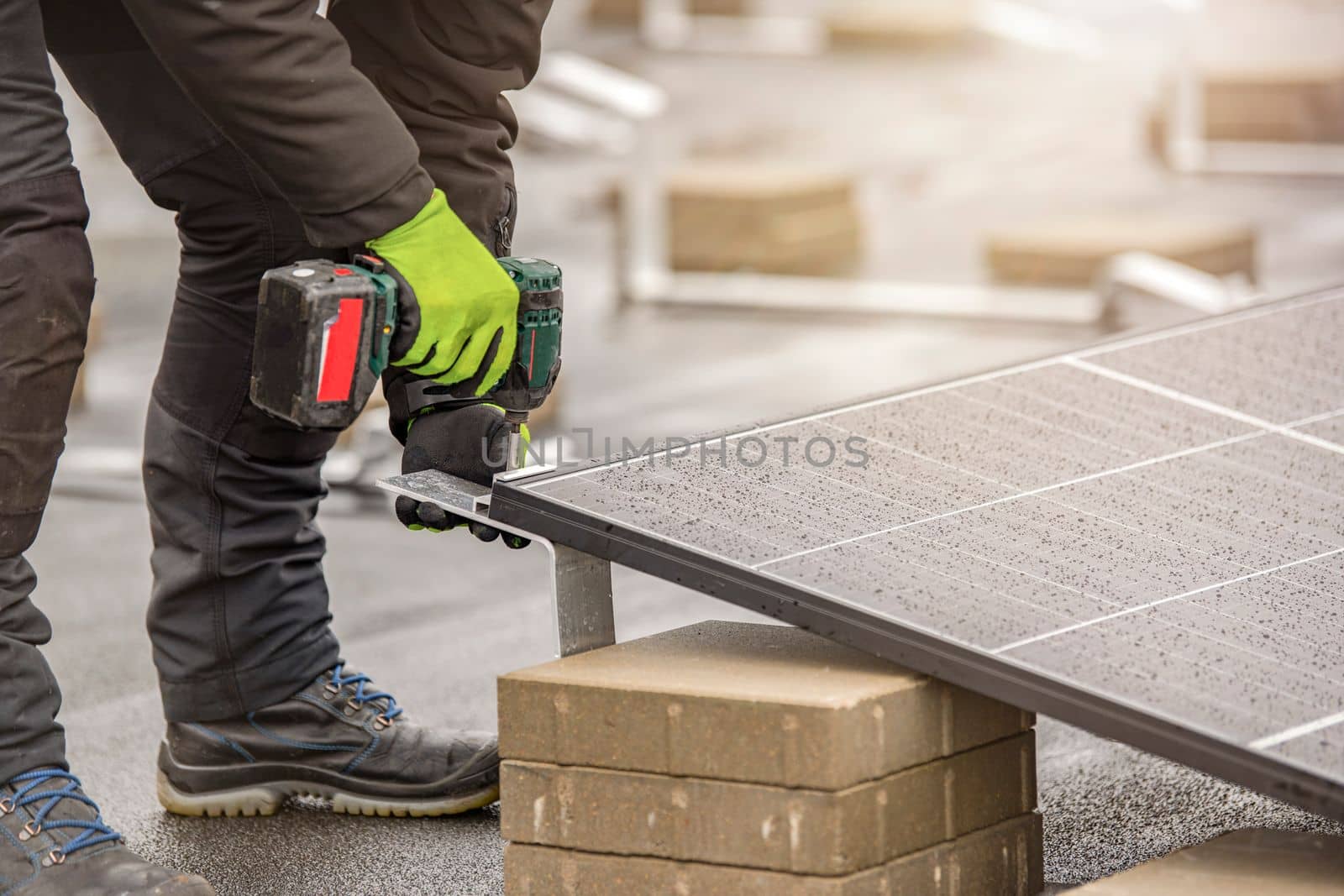 The solar panel installer twists the modules together using aluminum fasteners and a cordless drill. Rooftop installation work and security, concept with copy space.