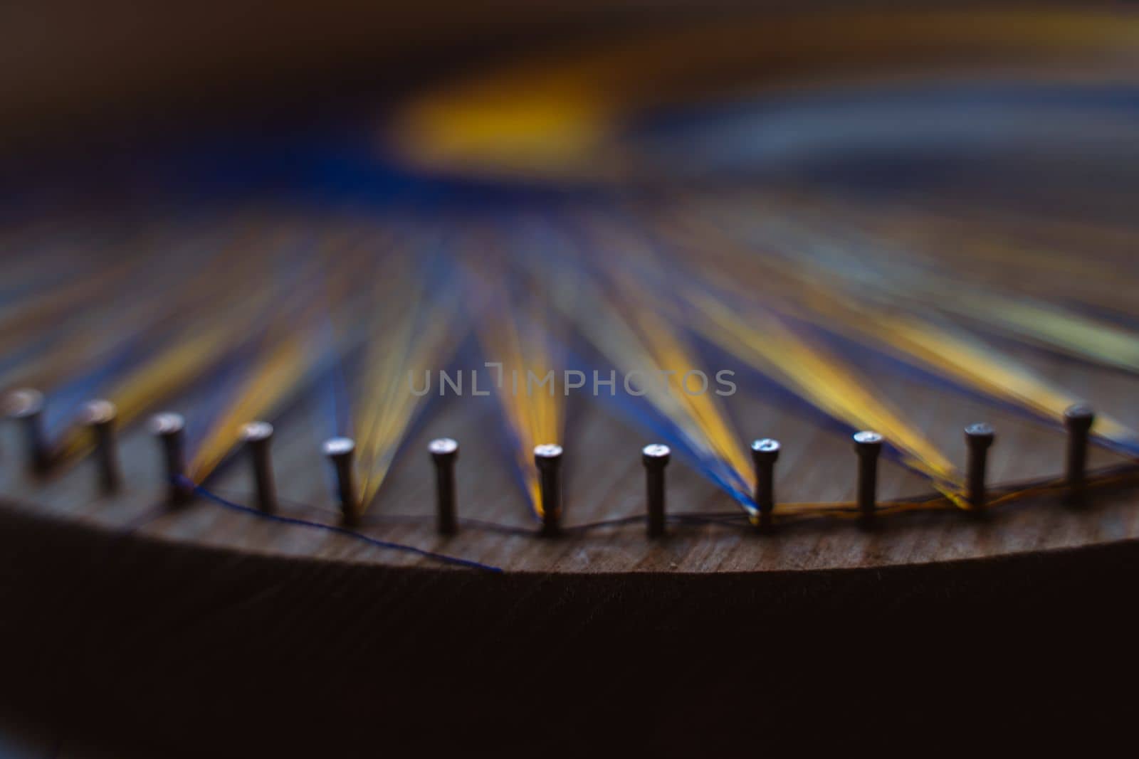 Colored thread mandala on a wooden board with nails. Mandala Moon Harmony Sun esotericism and psychology pictures from yellow and blue silk threads