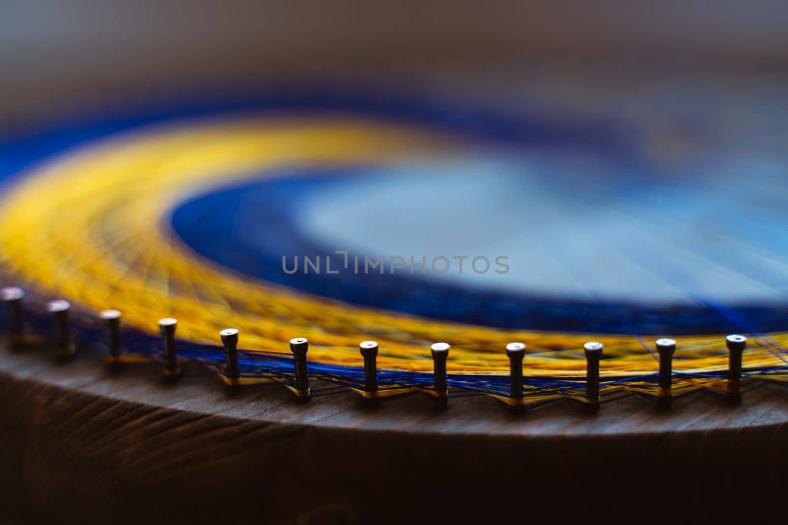 Colored thread mandala on a wooden board with nails. Mandala Moon Harmony Sun esotericism and psychology pictures from yellow and blue silk threads