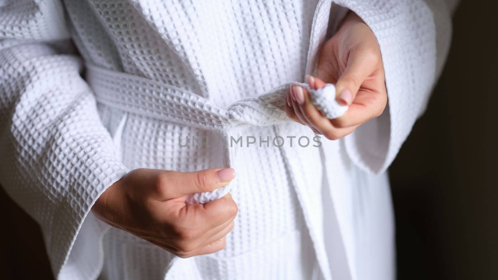 Female hands tying white bath robe closeup. Comfortable clothes for home concept