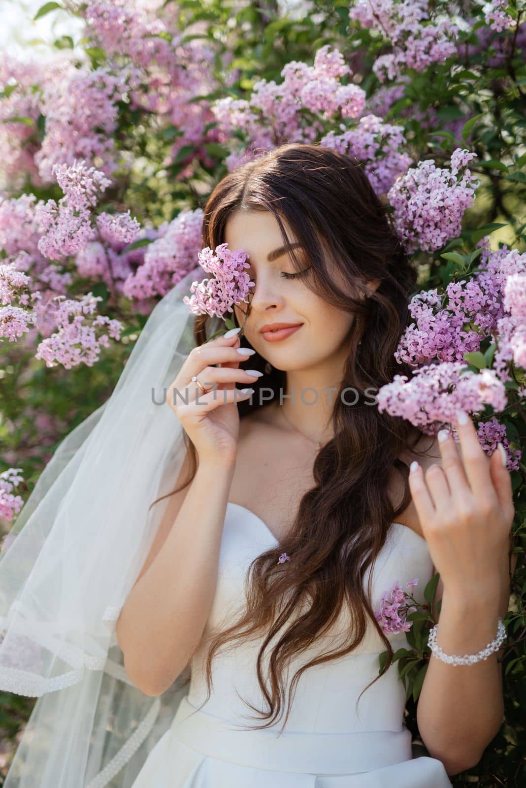 young girl bride in a white dress in a spring forest in lilac bushes on a wedding day