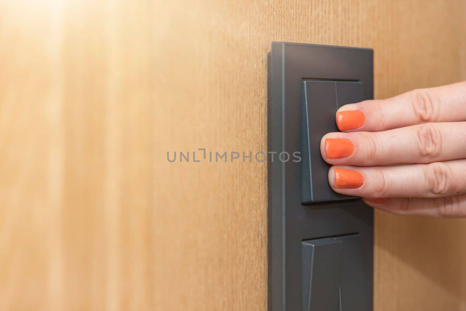 Turn on the light, a woman's hand presses the switch in the apartment close-up. Black light switch on the background of a wooden wall. The concept of saving electricity, the cost of electricity. by SERSOL