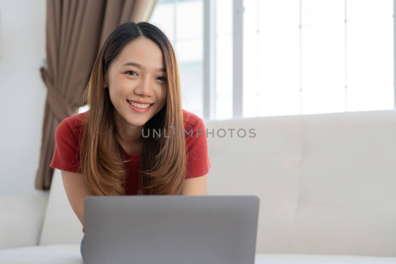An attractive young woman is working on a laptop while sitting on sofa at home.