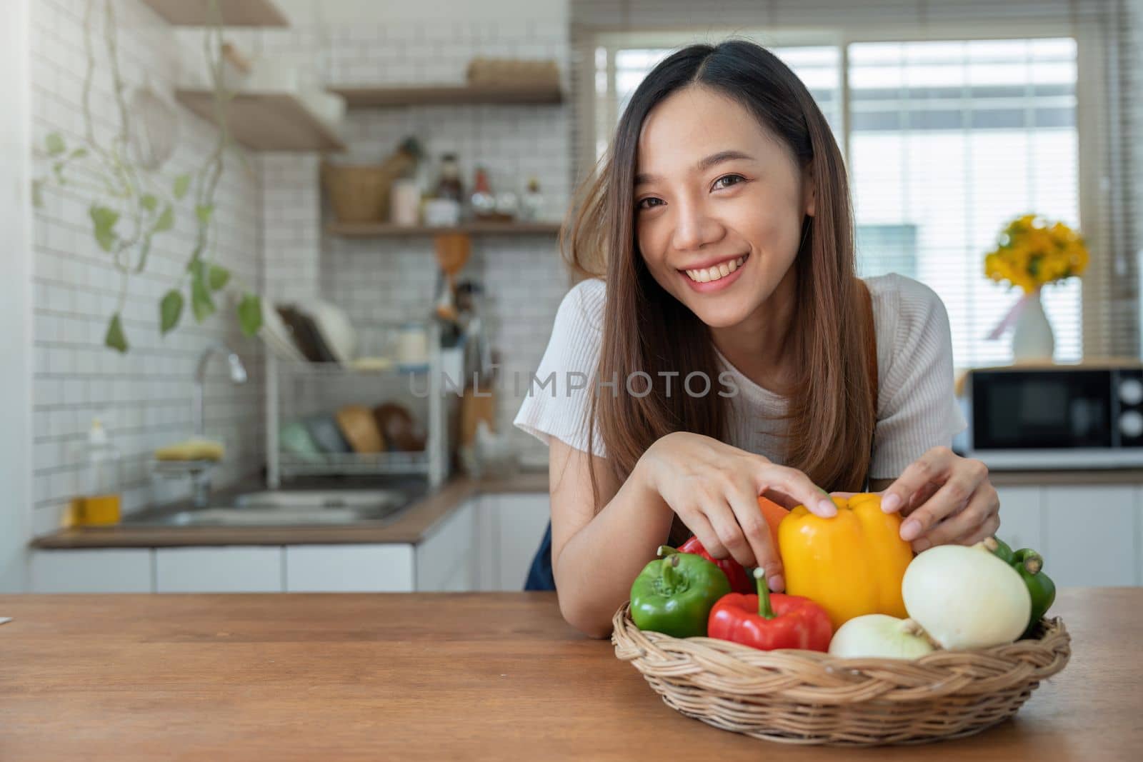 Portrait of Asian young woman look at camera. Attractive beautiful woman wear apron in cozy kitchen with fresh organic vegetables on table cooking healthy vegetable salad, healthy food active life by nateemee