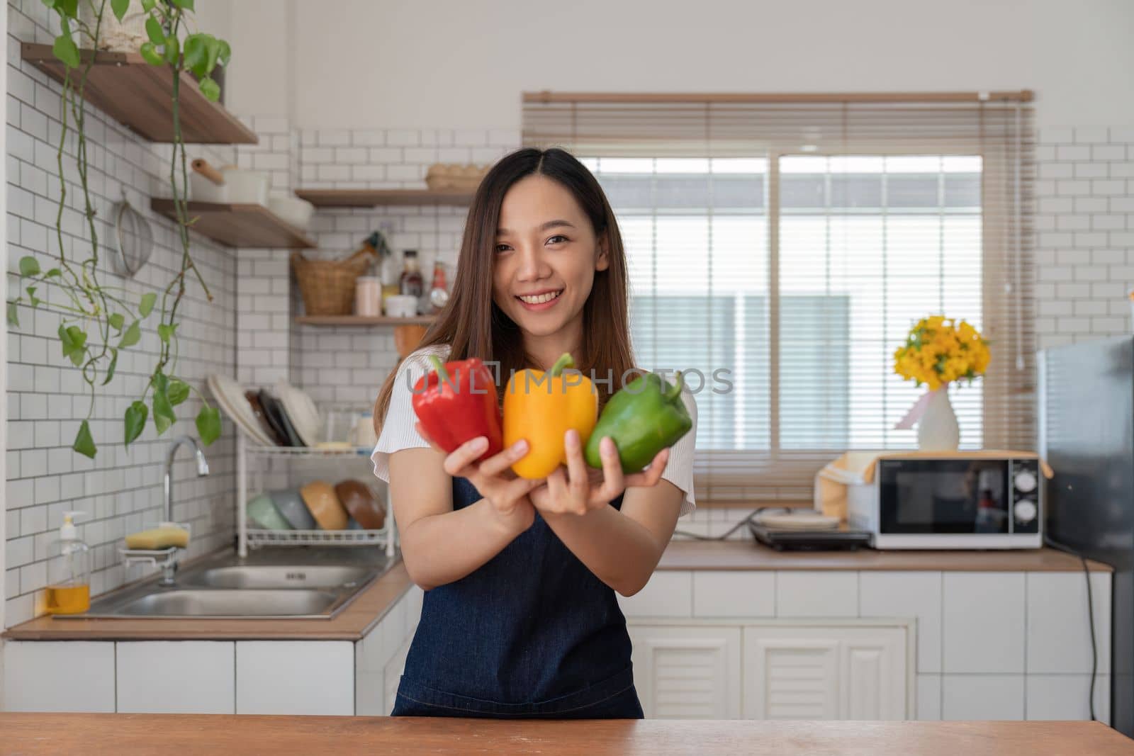 Portrait of Asian young woman look at camera. Attractive beautiful woman wear apron in cozy kitchen with fresh organic vegetables on table cooking healthy vegetable salad, healthy food active life by nateemee