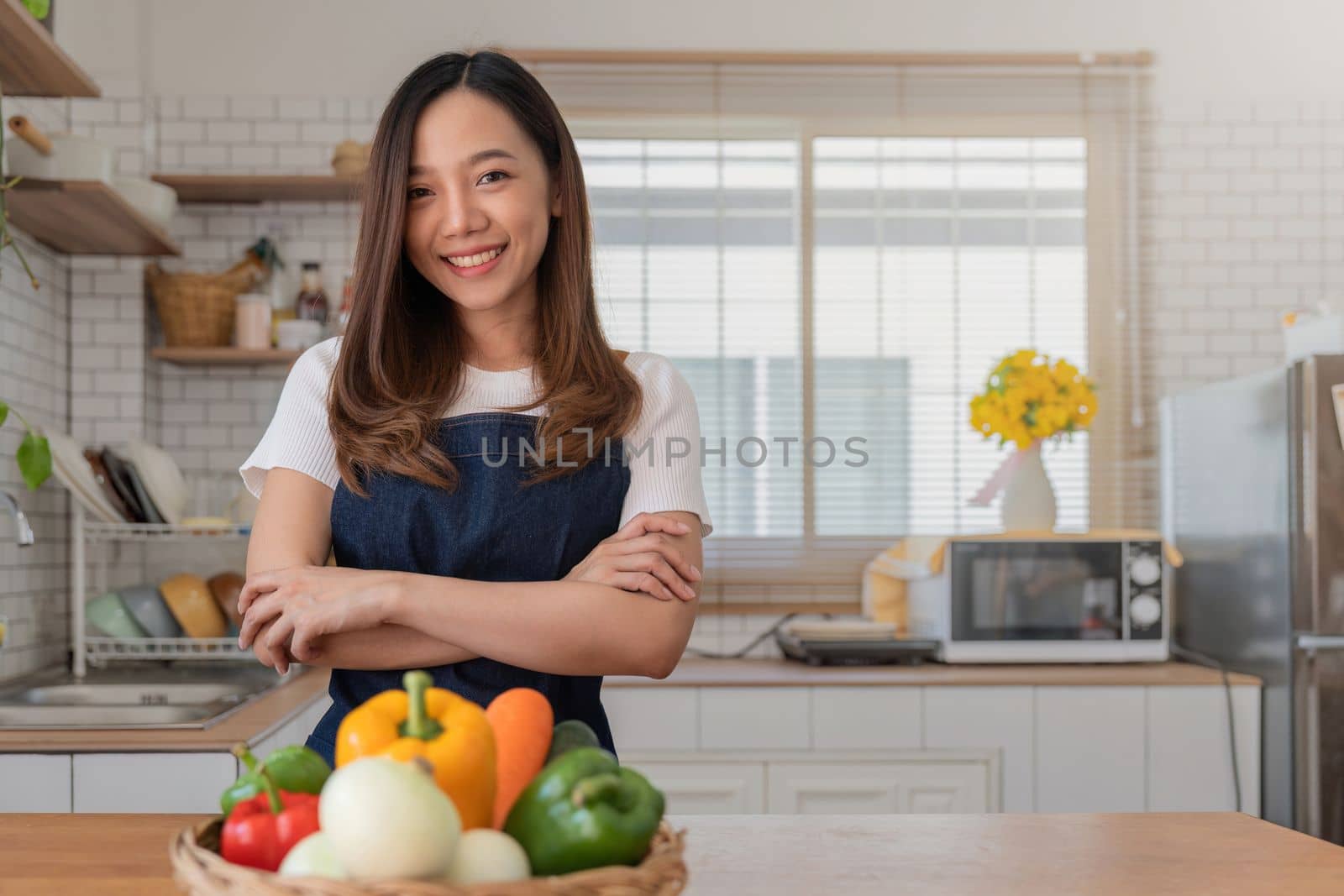 Portrait of Asian young woman look at camera. Attractive beautiful woman wear apron in cozy kitchen with fresh organic vegetables on table cooking healthy vegetable salad, healthy food active life.