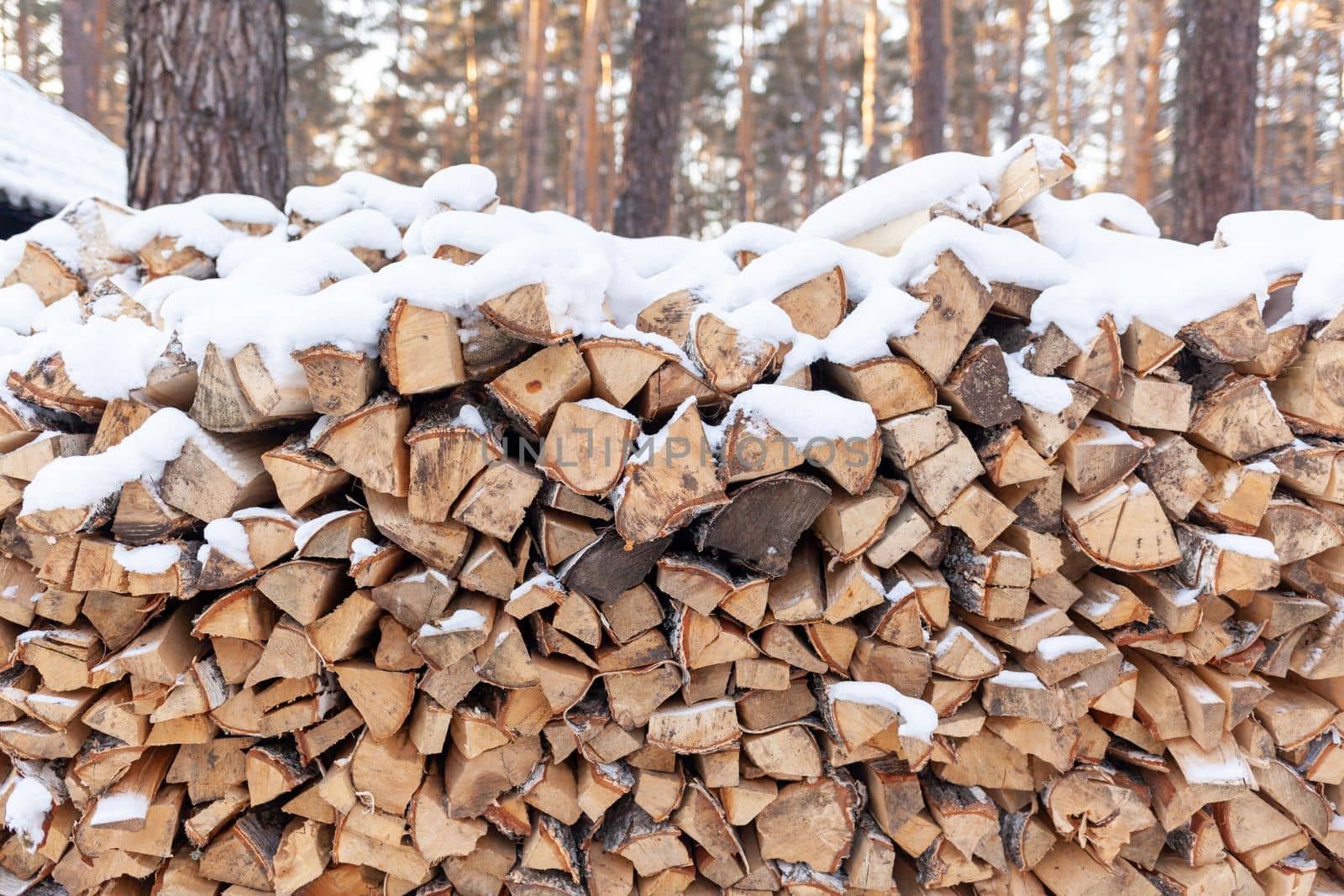 Stacked firewood covered with white snow, wood for kindling and heating. woodpile with stacked firewood birch tree covered fresh icy frozen snow and snowflakes. cold weather and snowy winter