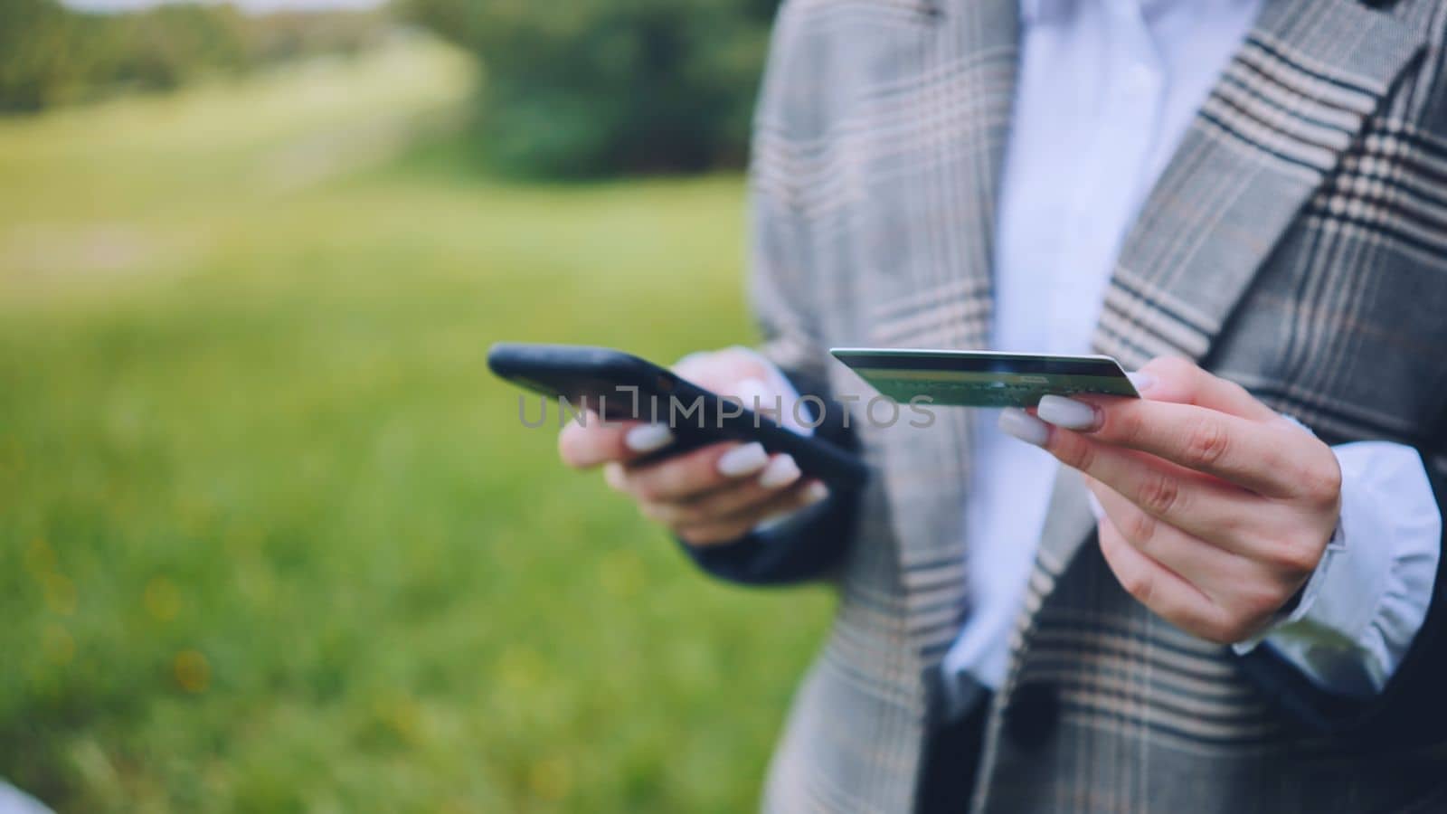 A young business lady makes a purchase with her phone and bank card in the park