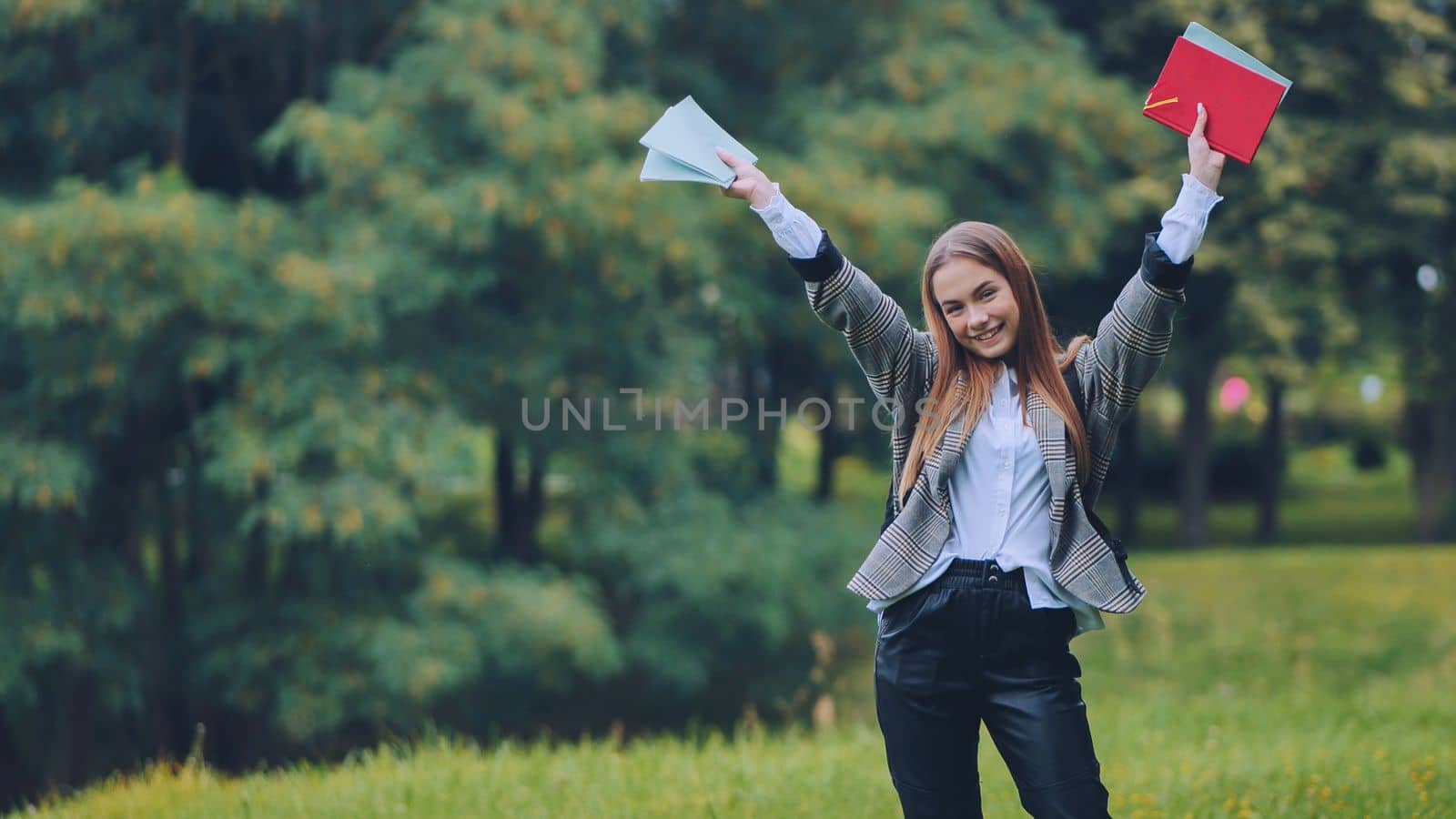 A cheerful student with books in the park in the summer