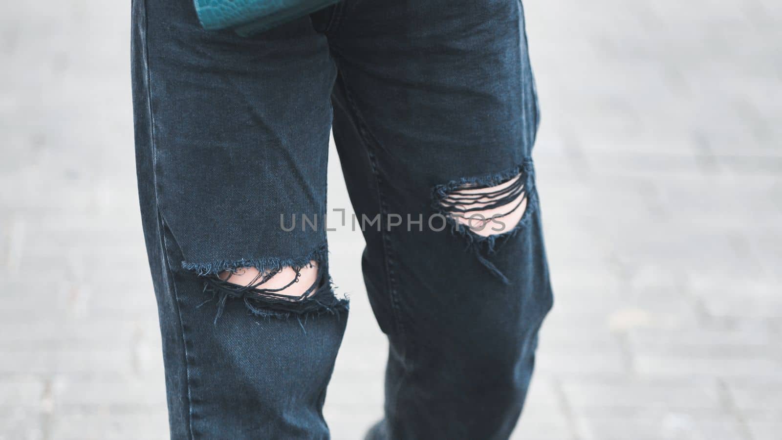 A girl in torn jeans walks through the city