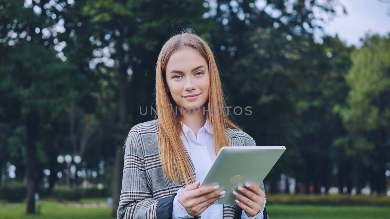 A young girl walks with a tablet in the park