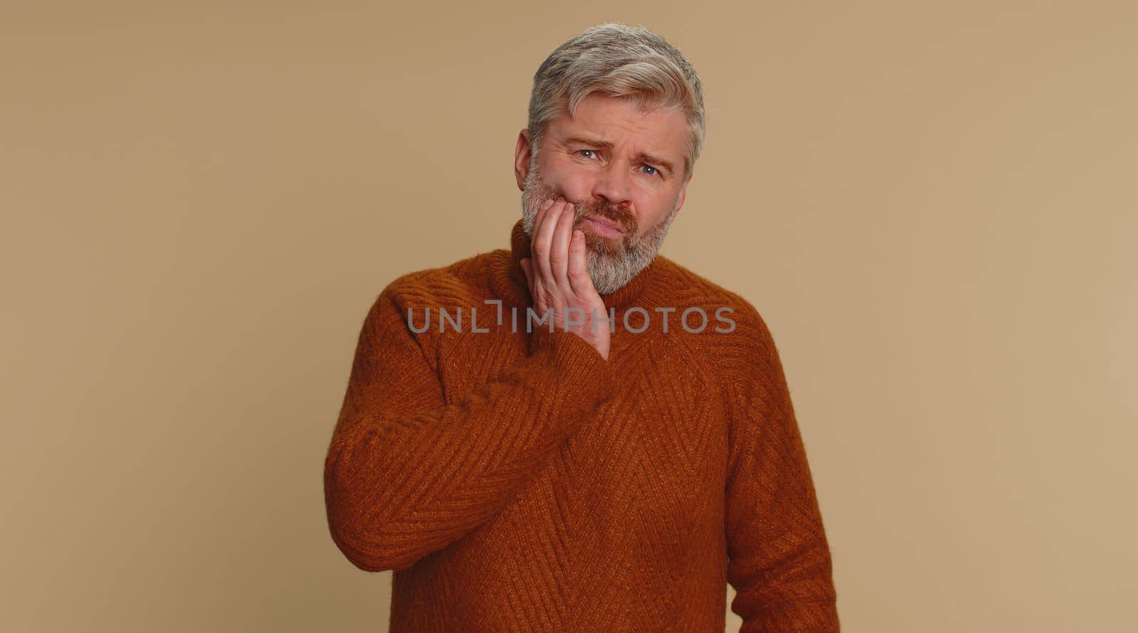 Middle-aged man touching sore cheek suffering from toothache cavities or gingivitis waiting for dentist appointment gums disease. Senior mature guy indoor studio shot isolated on beige background