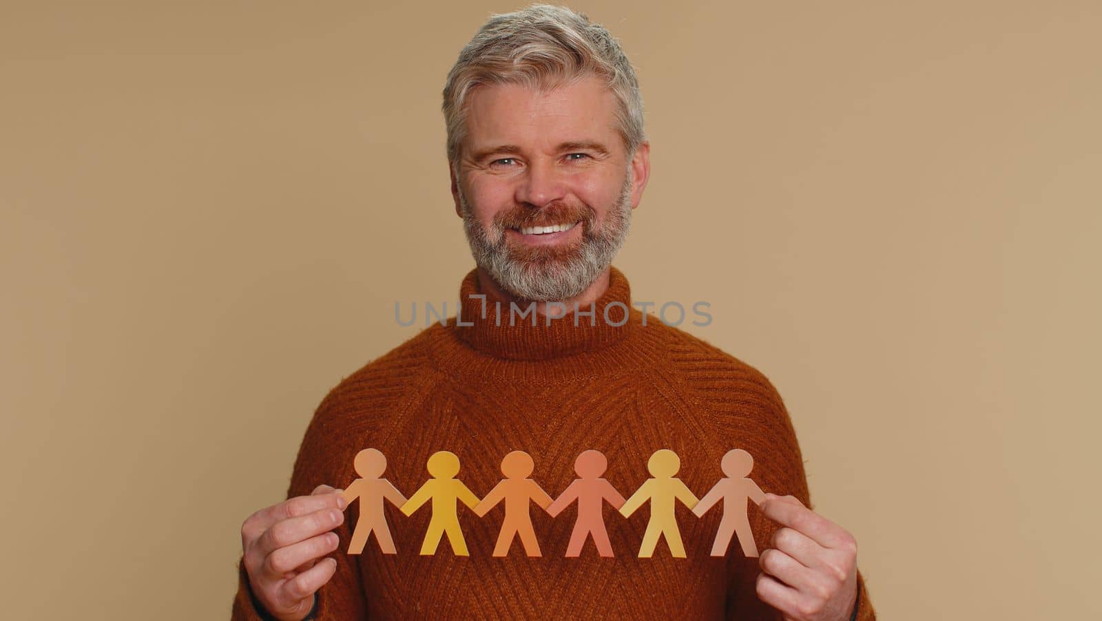 Man showing multiracial different skin color human shape cut out of paper, concept of teamwork, partnership, community, unity, people support love, against racism. Senior old guy on beige background