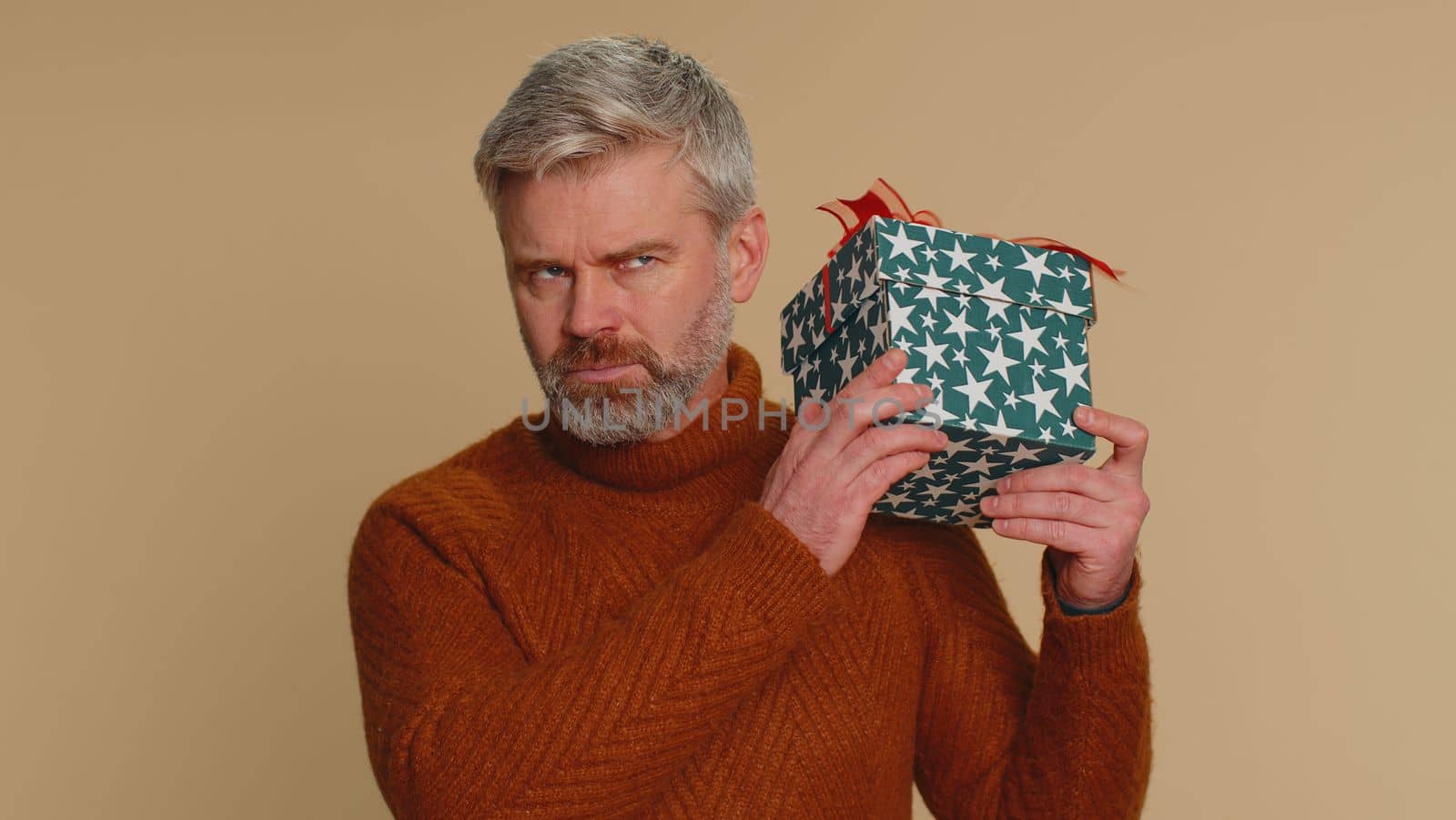 Happy middle-aged man opening gift box, unwrapping birthday surprise and expressing great happiness amazement, satisfied with best present bonus. Senior mature guy isolated on beige studio background