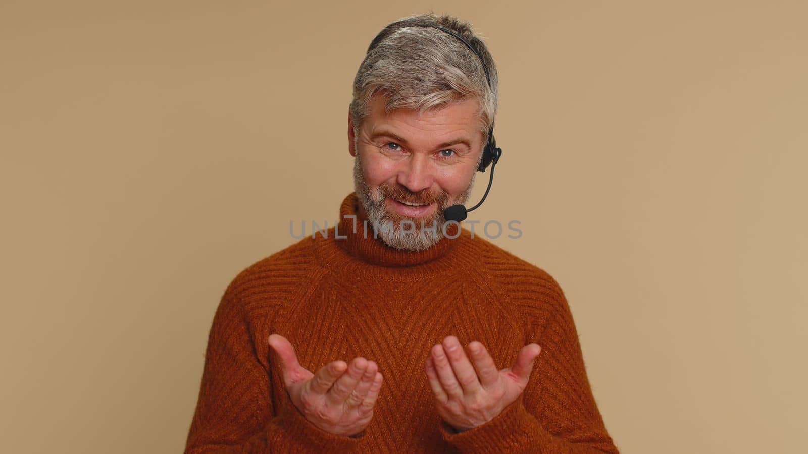 Smiling middle-aged man wearing headset, freelance worker, call center or support service operator helpline, having talk with client or colleague, communication support. Senior guy on beige background