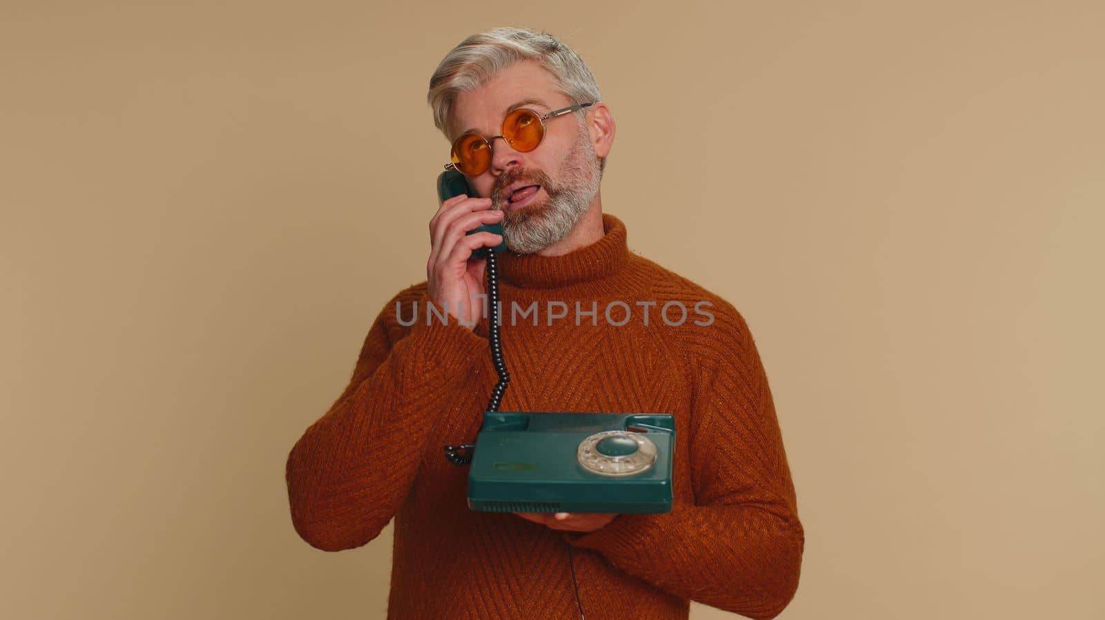 Bored tired middle-aged old man talking on wired vintage old-fashioned telephone of 80s, fooling making silly faces, not interested in communication talk, displeasure, uninteresting. Senior mature guy
