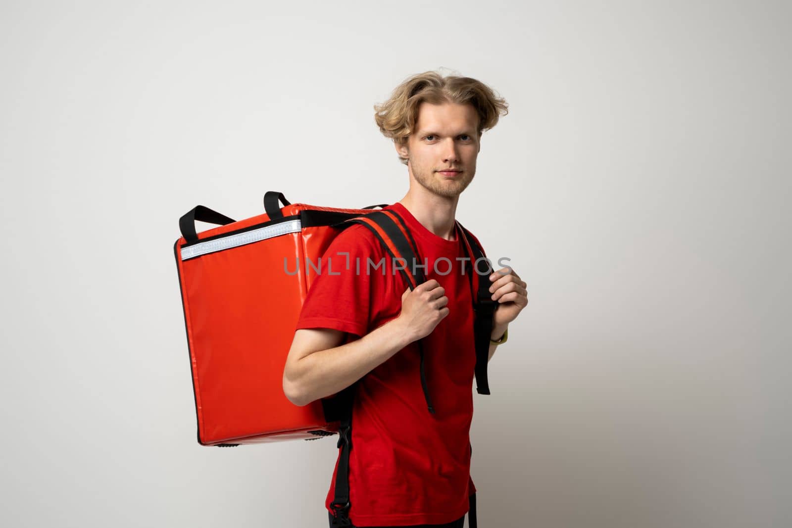 Young courier delivery man in red uniform with thermo bag isolated on white background. Delivery service