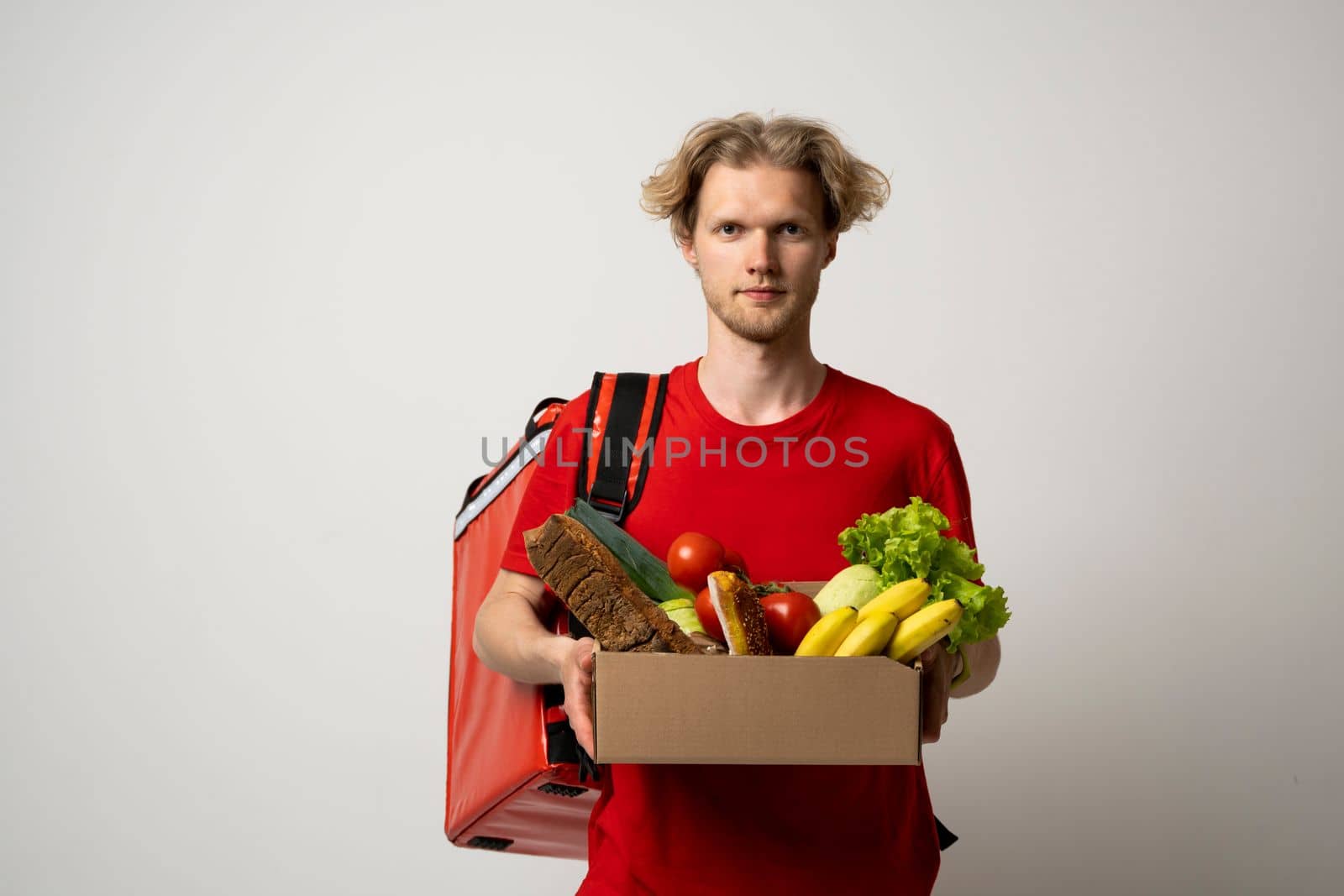 Delivery man in red uniform delivering food, groceries, vegetables, drinks in a paper box to a client at home. Online grocery shopping service concept
