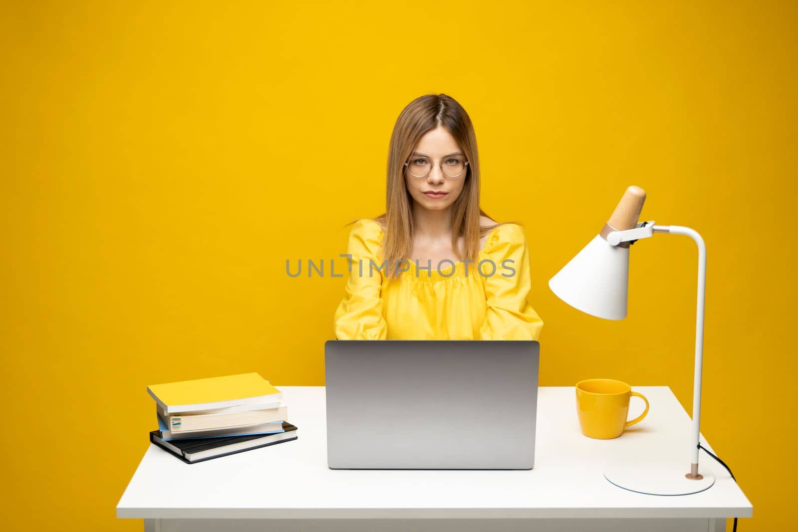 Young blonde freelancer woman in a yellow shirt using laptop for remote work, e-learning at university college, e-banking, online shopping, webinars. Yellow bakcground