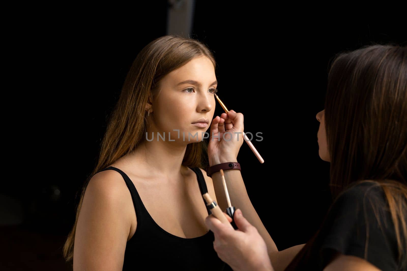A beautiful young woman with long hair doing makeup for a wedding or photo shoot. Work of a make-up artist. The morning of the bride. Decorative cosmetics. by vovsht