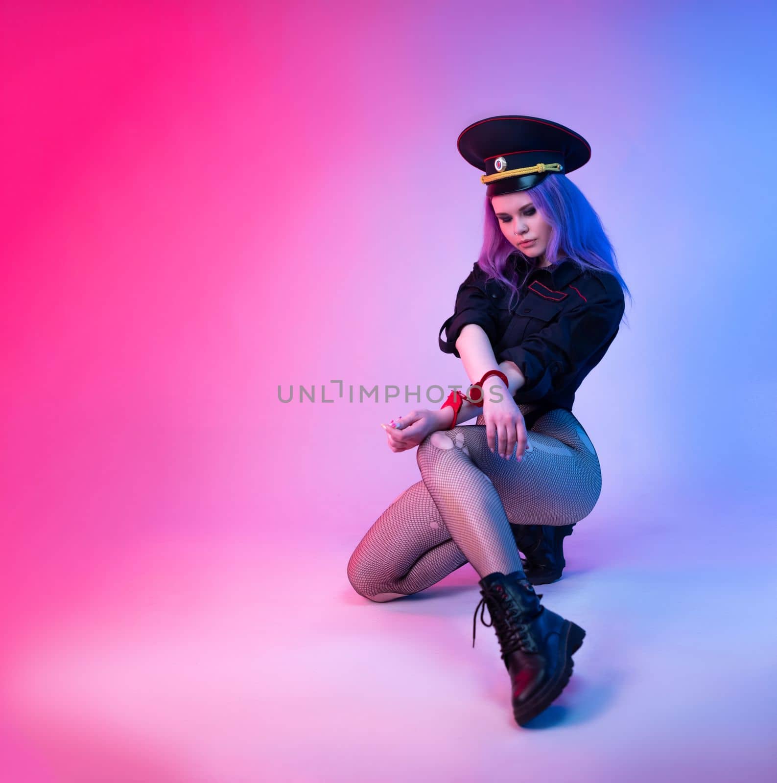 Sexy girl in police uniform for sexual games with handcuffs in neon light on the light background