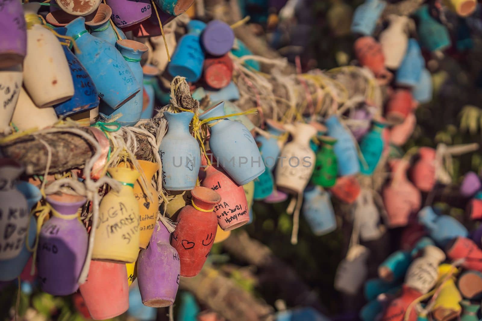 Wish tree. Small multi-colored jugs with inscriptions, wishes hanging on the branches of a tree., against the backdrop of sand ruins and blue sky.