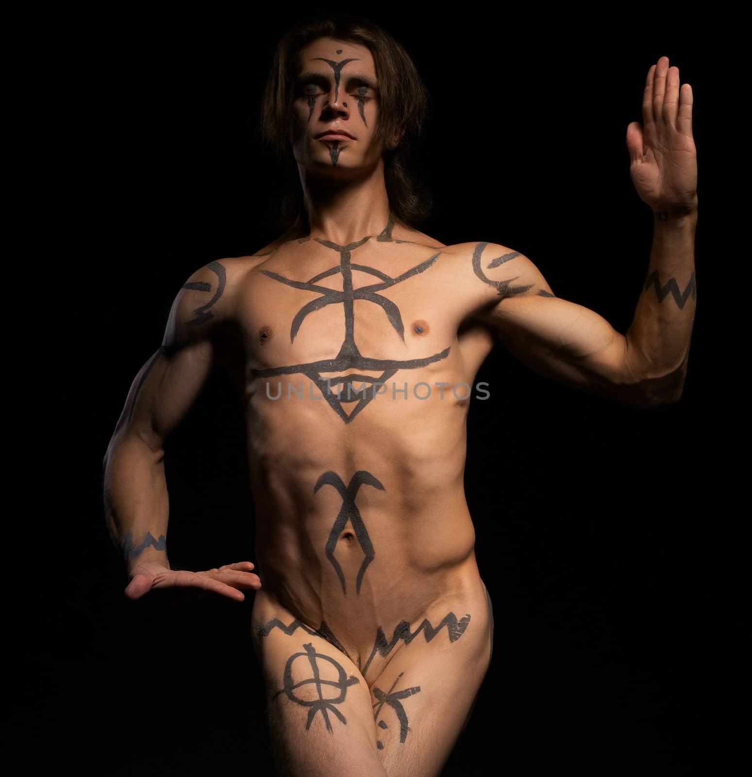 Young handsome man with bodyart dancing in the nude against black wall